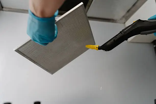 Shooting from below of cleaning service worker wearing gloves disinfecting kitchen extractor filter with steam cleaner, ensuring hygiene and cleanliness. Concept of modern housekeeping appliance.